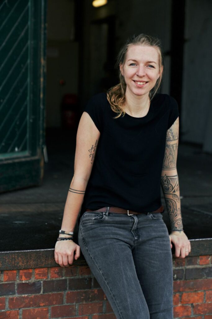 Porträt der Moderatorin Luisa Häußer in Jeans und T-Shirt vor Industriegebäude in Hamburg